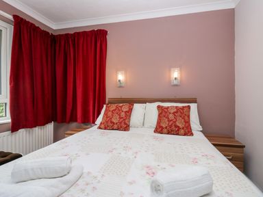 A bedroom with a double bed with floral bedding two red patterned cushions and white rolled towels on the bed at The Lodge in Ambleside