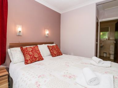 A bedroom with a bed with red pillows and rolled towels next to a bathroom at The Lodge in Ambleside