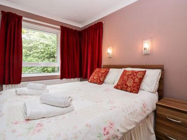 A bedroom with a double bed red pillows and curtains and a wooden bedside table at The Lodge in Ambleside