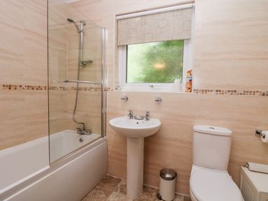 A bathroom with a bathtub shower combination sink toilet window and trash bin at The Lodge in Ambleside