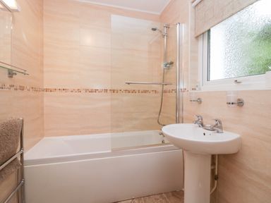 A bathroom with a bathtub shower combination and a sink under a frosted window at The Lodge in Ambleside