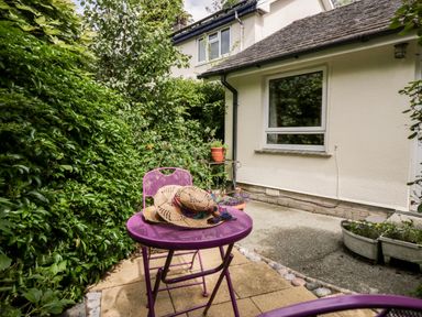 A small garden patio with a purple metal table and chair two straw hats on the table plants around the patio at The Lodge in Ambleside