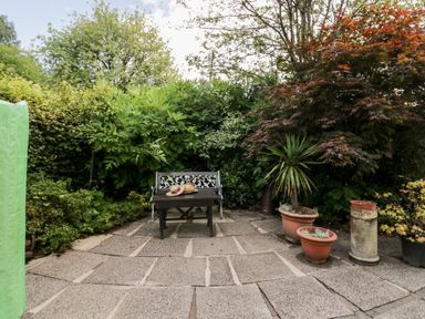 A garden patio with a bench and table surrounded by various plants and potted trees at The Lodge in Ambleside