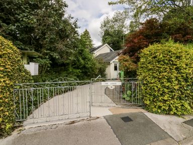 A driveway with metal gates and dense green foliage around a house at The Lodge in Ambleside