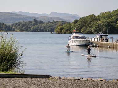 A lake with two people paddleboarding near moored boats and a dock at The Lodge in Ambleside