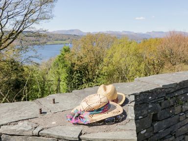 Two straw hats and a pair of sunglasses on a stone wall with trees and a lake in the background at The Lodge in Ambleside