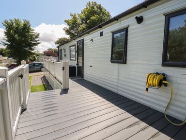 A deck with railing attached to a mobile home with windows and a hose reel at Pams Place in Crantock