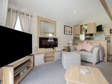 A living room with a sofa and ottoman next to a wood entertainment unit with a mounted electric fireplace and a television at Pams Place in Crantock