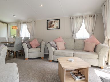 A living room with gray sofas pink cushions a wooden coffee table and a dining table with chairs at Pams Place in Crantock