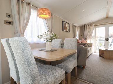 A dining area with a wooden table and patterned chairs next to a living room with a sofa and glass doors at Pams Place in Crantock
