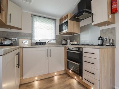 A kitchen with cabinets a stove a microwave a toaster and a window with blinds at Pams Place in Crantock
