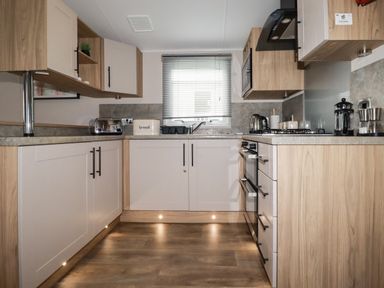 A kitchen with wooden cabinets a toaster a bread box a kettle a gas stove and a window with blinds at Pams Place in Crantock