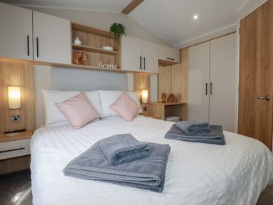 A bedroom with a double bed with folded towels on it pink pillows on the bed built in cupboards and shelves with decorations at Pams Place in Crantock
