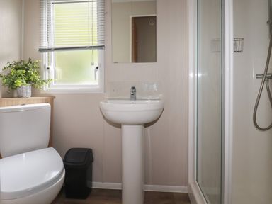 A bathroom with a toilet a pedestal sink a shower and a window with blinds at Pams Place in Crantock