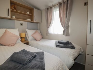 A bedroom with two single beds with gray towels on them a small lamp between the beds and a window with checked curtains at Pams Place in Crantock