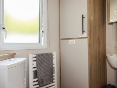 A bathroom with a toilet a heated towel rail with a towel a frosted window and a cupboard with warning signs at Pams Place in Crantock