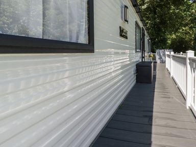 A side view of a mobile home with a wooden deck and white railing at Pams Place in Crantock