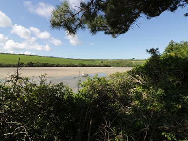 A river with boats near a sandy shore and green fields with trees under a blue sky at Pams Place in Crantock