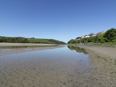 A sandy riverbank with water and houses on the hill at Pams Place in Crantock