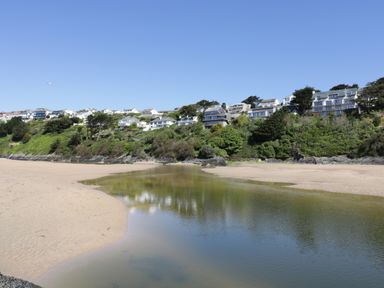 A sandy beach with a calm body of water in front of houses on a green hillside at Pams Place in Crantock
