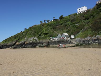 A sandy beach with small buildings on a rocky green hillside at Pams Place in Crantock