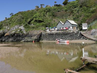 A small boat on water near a stone wall and grey buildings by a green hillside at Pams Place in Crantock