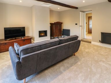 A living room with a gray sofa a TV on a wooden chest a built-in fireplace and wooden cabinet at Luham Cottage Edenhall near Langwathby