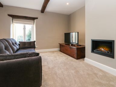 A living room with a dark sofa a television on a wooden chest and a wall-mounted fireplace at Luham Cottage Edenhall near Langwathby