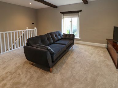 A living room with a dark sofa a window and a television on a wooden stand at Luham Cottage Edenhall near Langwathby