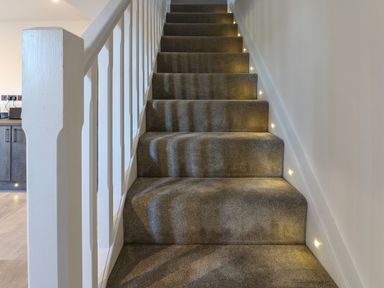 A carpeted staircase with white railing and small lights along the wall at Luham Cottage Edenhall near Langwathby