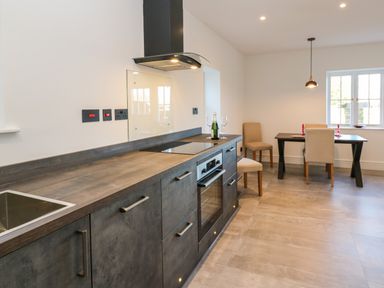 A kitchen with dark cabinets and countertop adjacent to a dining area with a table and chairs at Luham Cottage in Edenhall near Langwathby