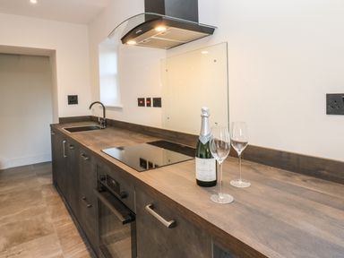 A kitchen countertop with a bottle of champagne and two wine glasses near a stove and sink at Luham Cottage in Edenhall near Langwathby