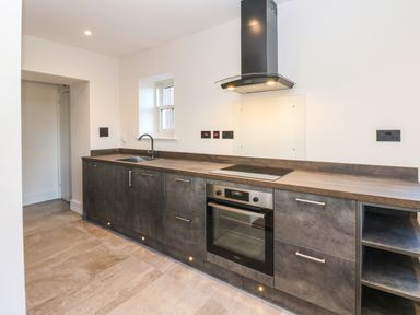 A kitchen with dark cabinets a built-in oven stovetop and a sink at Luham Cottage in Edenhall near Langwathby