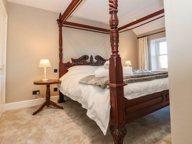 A bedroom with a carved wooden four-poster bed two small lamps on side tables and a window with curtains at Luham Cottage Edenhall near Langwathby