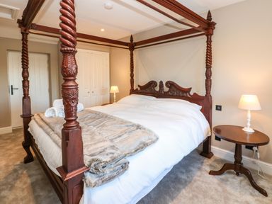 A bedroom with a carved wooden four poster bed bedside tables with lamps and a closed closet at Luham Cottage Edenhall near Langwathby