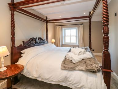 A bedroom with a wooden four-poster bed white bedding a wooden side table with a lamp and a window with curtains at Luham Cottage Edenhall near Langwathby