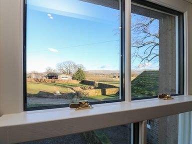 A view through a window showing a rural landscape with fields trees a stone wall and farm buildings at Luham Cottage Edenhall near Langwathby