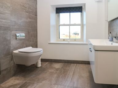 A bathroom with a wall-mounted toilet and a sink under a window at Luham Cottage in Edenhall near Langwathby