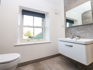 A bathroom with a toilet, window, sink, mirror, and soap dispenser at Luham Cottage in Edenhall near Langwathby