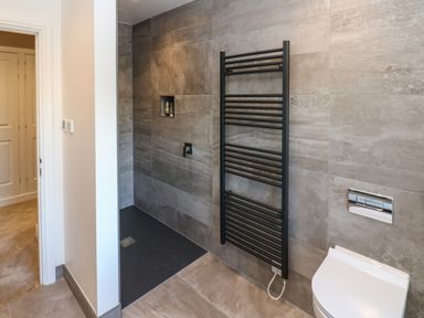 A bathroom with a walk-in shower, black towel radiator, and a white wall-mounted toilet at Luham Cottage Edenhall near Langwathby