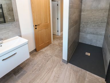 A bathroom with a wooden door a white sink and a walk in shower area with tiled walls at Luham Cottage in Edenhall near Langwathby