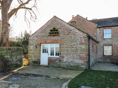 The exterior of a stone cottage with a white door and windows by a stone wall and a large tree at Luham Cottage Edenhall near Langwathby