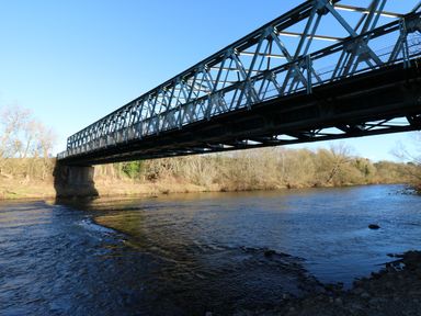 A metal truss bridge over a river with trees along the riverbank at Luham Cottage in Edenhall near Langwathby