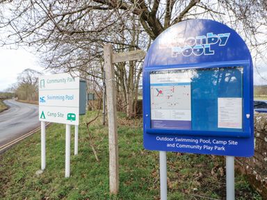 Roadside signs including a blue informational sign for Lazonby Pool and a white sign for community park swimming pool and camp site at Luham Cottage Edenhall near Langwathby