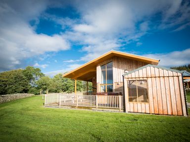 A wooden cabin with a fenced porch in a grassy area with trees at Aurae in Cawdor near Inverness