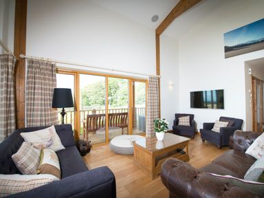 A living room with sofas armchairs coffee table and sliding glass doors at Aurae in Cawdor near Inverness