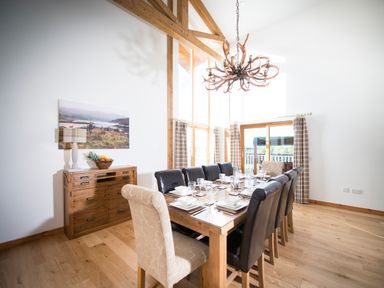 A dining room with a wooden table set with plates and glasses surrounded by chairs and a wooden sideboard with a lamp and fruit bowl at Aurae in Cawdor near Inverness