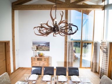 A dining room with a wooden table set for a meal and an antler chandelier at Aurae in Cawdor near Inverness