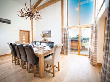 A dining room with a large wooden table and mixed upholstered chairs near a tall window with curtains at Aurae in Cawdor near Inverness