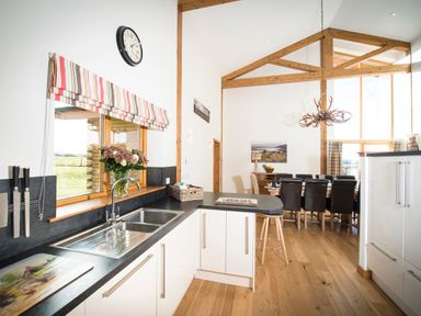 A kitchen with a sink counter and knives on the wall next to a dining area with a wooden table and chairs at Aurae in Cawdor near Inverness